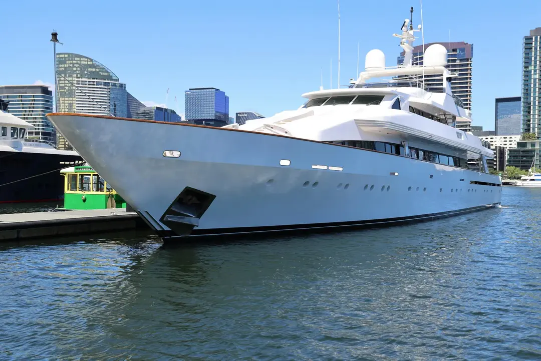 Large white motor yacht moored bow-on at a city marina with a modern skyline behind