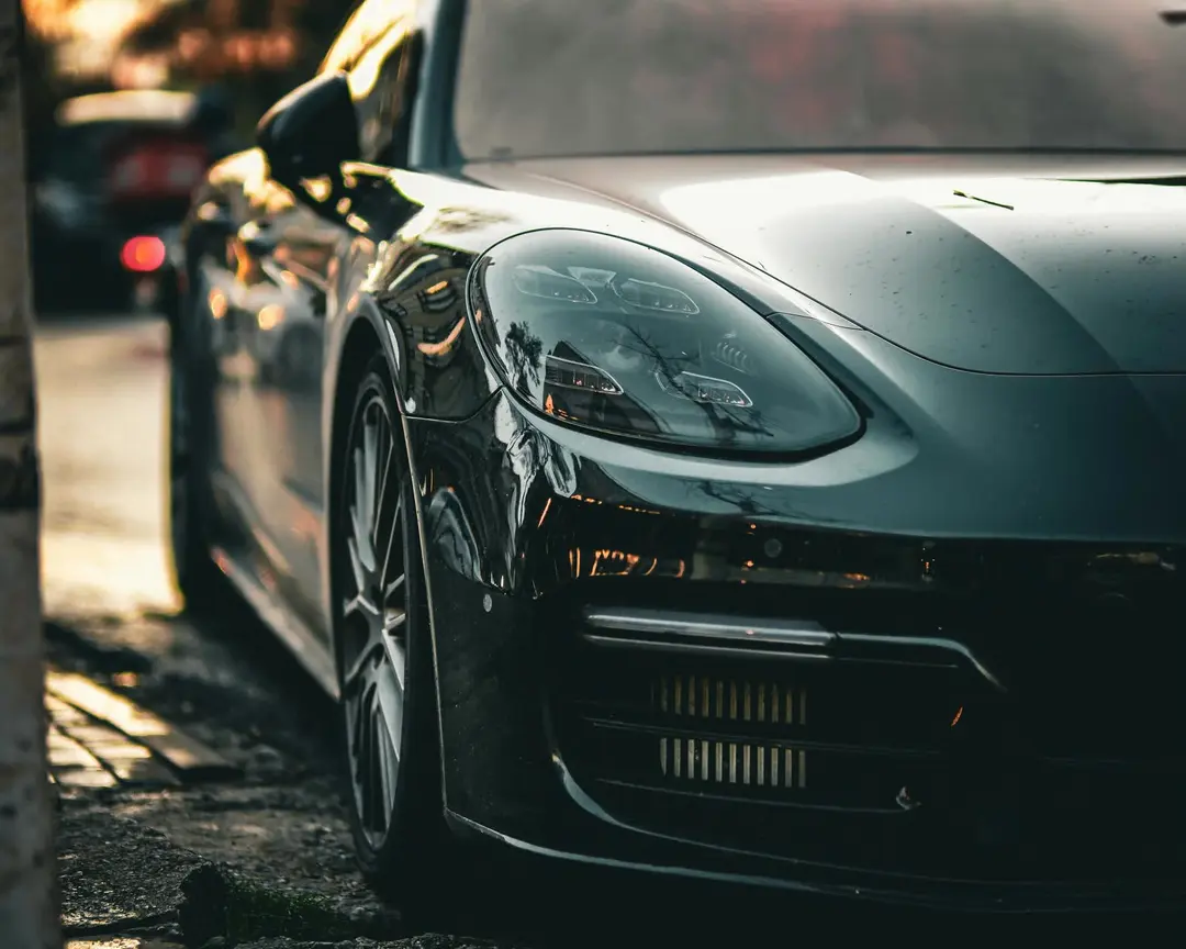 Front quarter of a dark sports sedan parked at a kerb in low golden light, headlight and alloy wheel in sharp focus
